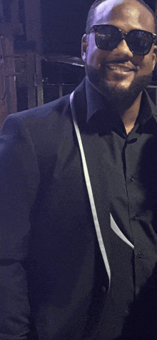 a man wearing sunglasses and a black suit smiles