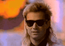 a man with a mullet wearing sunglasses and a white jacket