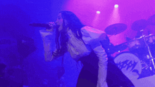 a woman is singing into a microphone on a stage in a purple light .