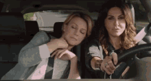 two women are sitting in the back seat of a car . one of the women is sleeping while the other is driving .