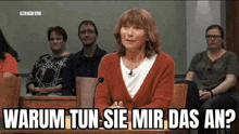 a woman in a red sweater is sitting at a table in front of a microphone in a courtroom .