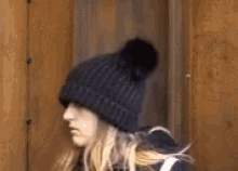 a woman wearing a black hat with a pom pom is standing in front of a rusty wall .
