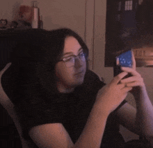 a woman wearing glasses is sitting in a chair holding a cell phone .
