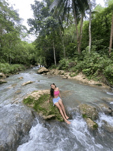 a woman sits on a rock in a river