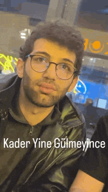 a man with glasses and a beard is wearing a leather jacket and looking at the camera .