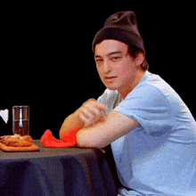 a man wearing a beanie is sitting at a table with a glass of water