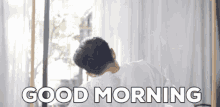 a man in a white shirt is saying good morning in front of a window .