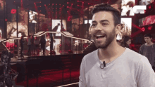 a man with a beard is smiling in front of a stage with a microphone .