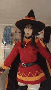 a woman in a witch costume is standing in a room wearing a red dress and a black hat .