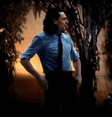 a man in a suit and tie is standing in front of a tree .