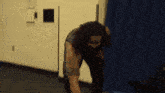 a man with long hair and a beard is standing in a room with a blue curtain behind him .