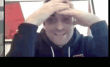 a man in a hoodie is smiling and holding his hands to his forehead .