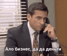 a man in a suit and tie is talking on a phone in a foreign language with makeitmeme.com at the bottom