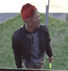 a man wearing a red hat and a black jacket is standing in a grassy area .