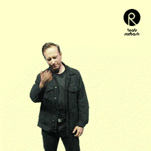 a man in a black denim jacket is standing in front of a yellow background with a logo for teatr rozbark on it