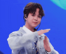 a young man wearing a tie and ear buds is clapping his hands