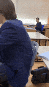 a man sits at a desk in a classroom with a blue chair