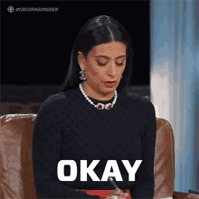 a woman is sitting in a chair with the word okay on her chest