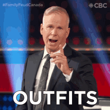 a man in a suit and tie says " outfits " while pointing