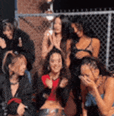 a group of women are sitting in front of a chain link fence and laughing .
