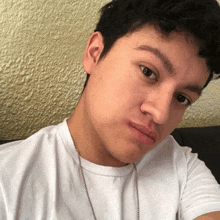 a young man wearing a white t-shirt and a necklace looks at the camera