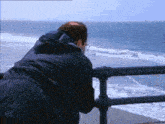 a man is leaning over a railing looking at the ocean .