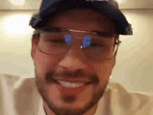 a man with a beard wearing glasses and a hat is smiling