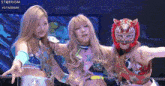 three female wrestlers are posing for a picture in a ring and one of them is wearing a tiger mask .