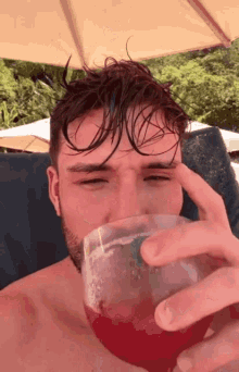 a shirtless man is drinking from a glass with a red liquid in it