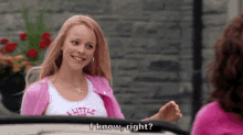 a woman is sitting in a car talking to another woman while wearing a pink cardigan .