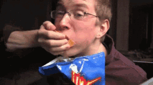 a man with glasses is eating a bag of nachos