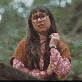 a woman wearing glasses and a sweater is standing in a forest