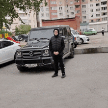 a man in a hooded vest is standing in front of a black mercedes