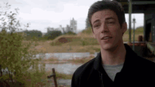 a man in a black jacket is standing in front of a pond .
