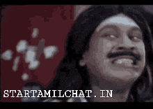 a man with long hair and a mustache is smiling and the words starttamilchat.in are below him