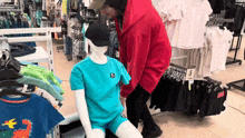 a man in a red hoodie adjusts a blue shirt on a mannequin in a clothing store