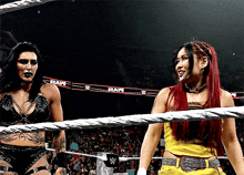 two women are standing in a wrestling ring with a banner that says raw