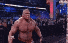 a very muscular wrestler is standing in front of a crowd in a wrestling ring .