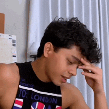 a young man with curly hair is wearing a black tank top that says london .