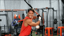 a man in a red tank top is swinging a baseball bat .