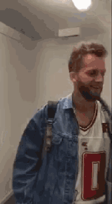 a man with a beard and a denim jacket is standing in a hallway .
