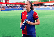 a woman in a soccer uniform is standing on a field holding a blue bottle .