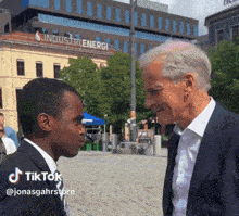 a man in a suit and tie is talking to another man in front of a building that says industrienergi