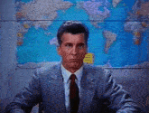 a man in a suit and tie is sitting in front of a world map .