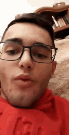 a man wearing glasses and a red shirt is making a face .