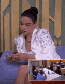 a woman in a white shirt is sitting on a couch looking at her phone