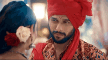 a man wearing a red turban is looking at a woman with a flower in her hair