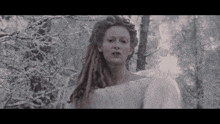 a woman with dreadlocks is standing in the woods wearing a white sweater .