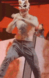 a man without a shirt is wearing a devil mask and dancing on a stage .