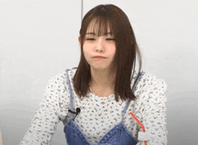 a young woman wearing a white shirt and blue overalls is making a funny face